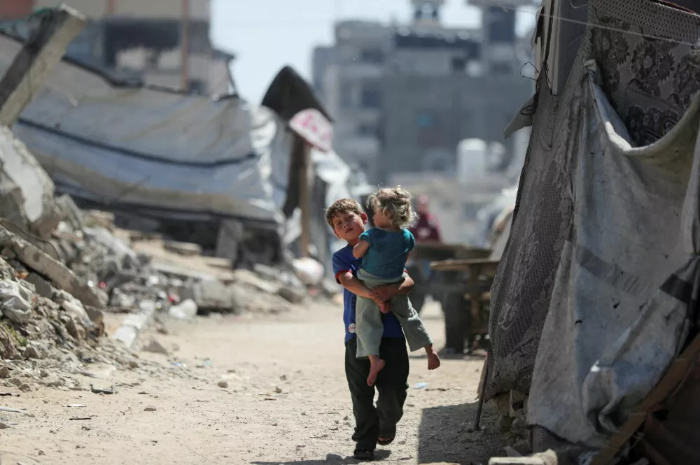 A Palestinian boy, carrying a girl child, walks through a damaged area amid the rubble of residential buildings in Gaza City, May 11, 2026. REUTERS/Dawoud Abu Alkas   TPX IMAGES OF THE DAY / Foto: Dawoud Abu Alkas