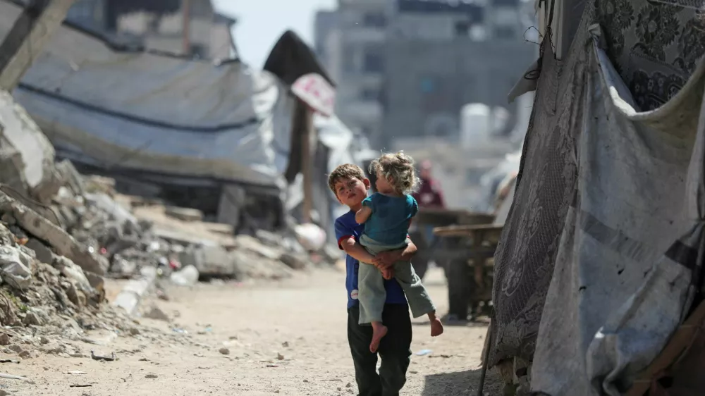 A Palestinian boy, carrying a girl child, walks through a damaged area amid the rubble of residential buildings in Gaza City, May 11, 2026. REUTERS/Dawoud Abu Alkas   TPX IMAGES OF THE DAY / Foto: Dawoud Abu Alkas