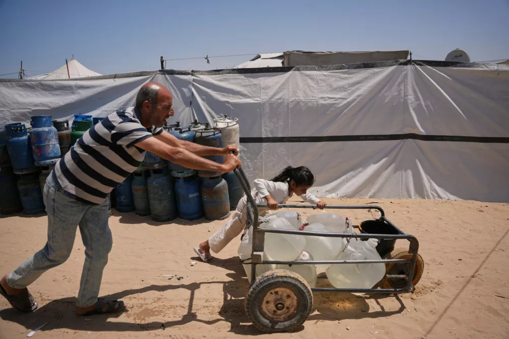 Ne'man Abu Jarad and his daughter push a cart loaded with jerrycans filled with water as they walk at a tent camp for displaced Palestinians in Khan Younis, southern Gaza Strip, Wednesday, May 13, 2026. (AP Photo/Abdel Kareem Hana)