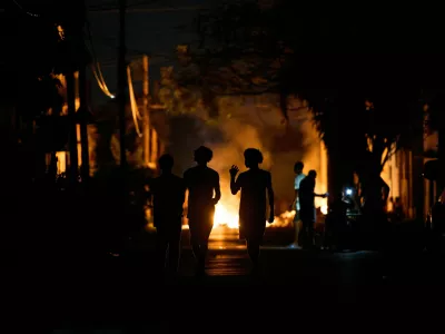 People walk down the street next to a fire set up by residents protesting against prolonged power outages on the street in Havana, Cuba, Thursday, May 14, 2026. (AP Photo/Ramon Espinosa)