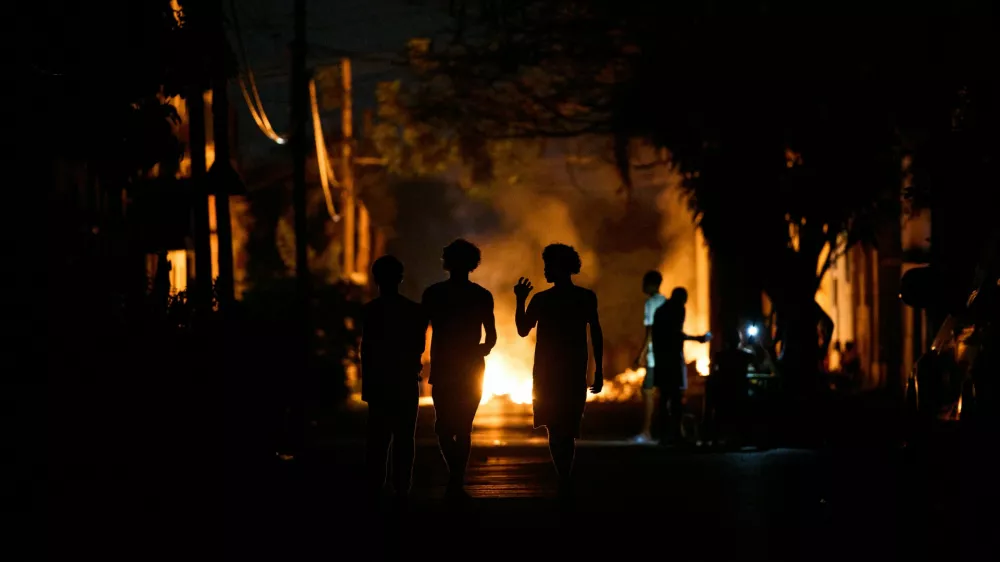 People walk down the street next to a fire set up by residents protesting against prolonged power outages on the street in Havana, Cuba, Thursday, May 14, 2026. (AP Photo/Ramon Espinosa)