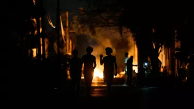 People walk down the street next to a fire set up by residents protesting against prolonged power outages on the street in Havana, Cuba, Thursday, May 14, 2026. (AP Photo/Ramon Espinosa)