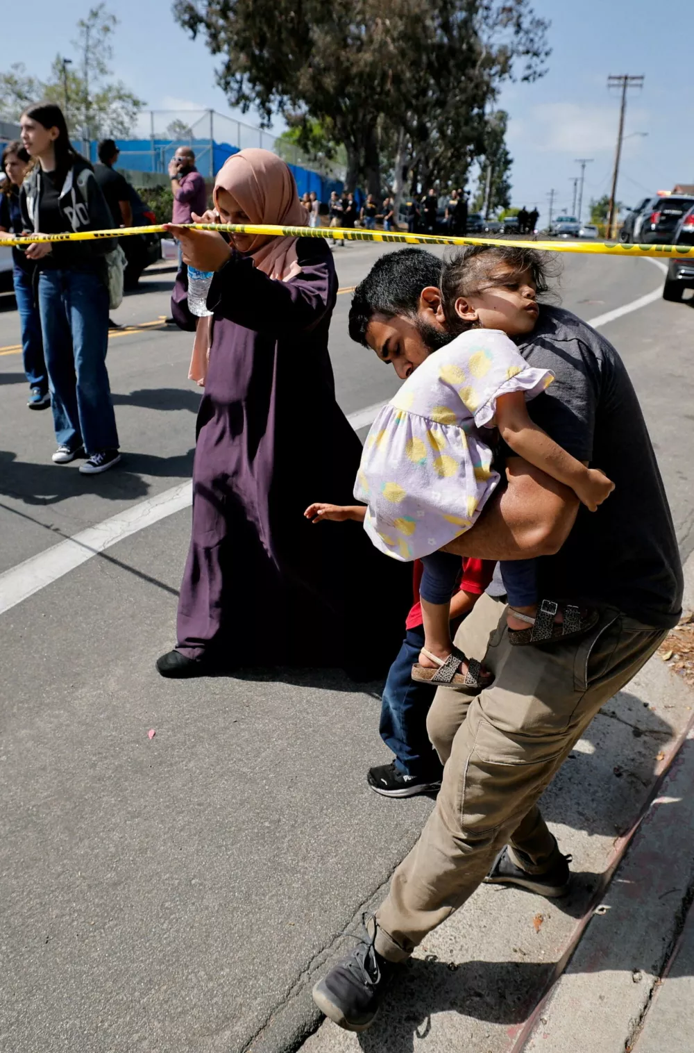 A parent passes under yellow tape cordoning an area, as he carries his child while they leave the mosque, at the scene of a shooting at the Islamic Center in San Diego, California, U.S., May 18, 2026. REUTERS/Mike Blake