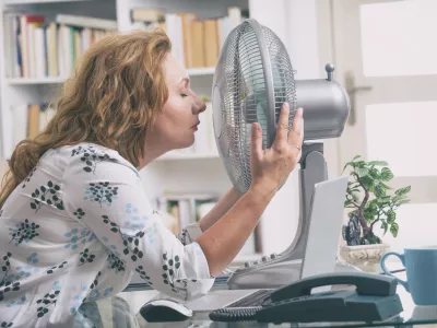Woman suffers from heat while working in the office and tries to cool off by the fan