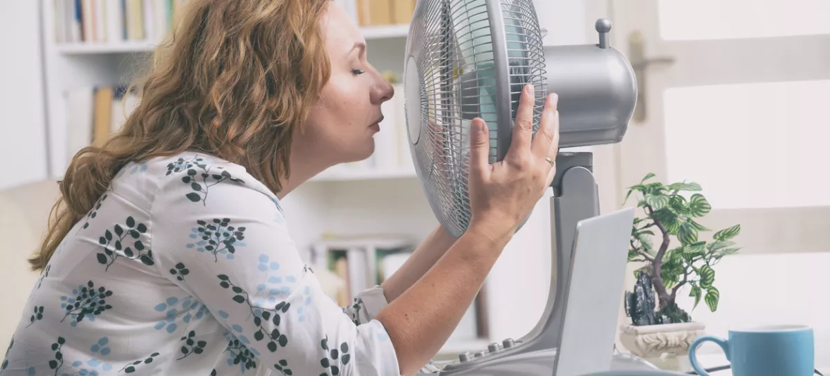 Woman suffers from heat while working in the office and tries to cool off by the fan