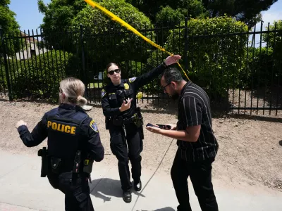People walk under police tape at the scene of a shooting outside the Islamic Center of San Diego Monday, May 18, 2026, in San Diego. (AP Photo/Gregory Bull)