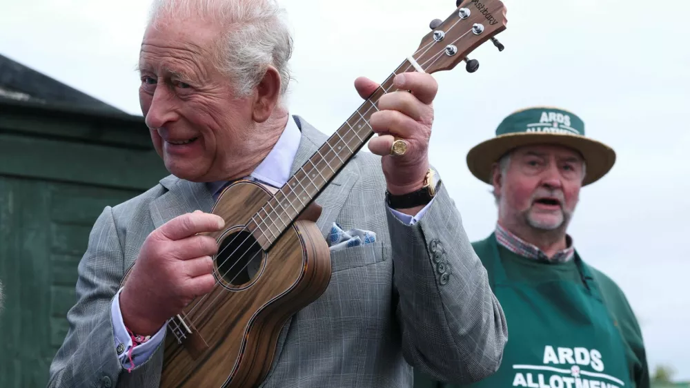 Britain's King Charles plays ukulele as the founder of Ards Allotments, Maurice Patton, looks on during his visit to Ards Allotments, in County Down, Northern Ireland, May 21, 2026. REUTERS/Toby Melville/Pool