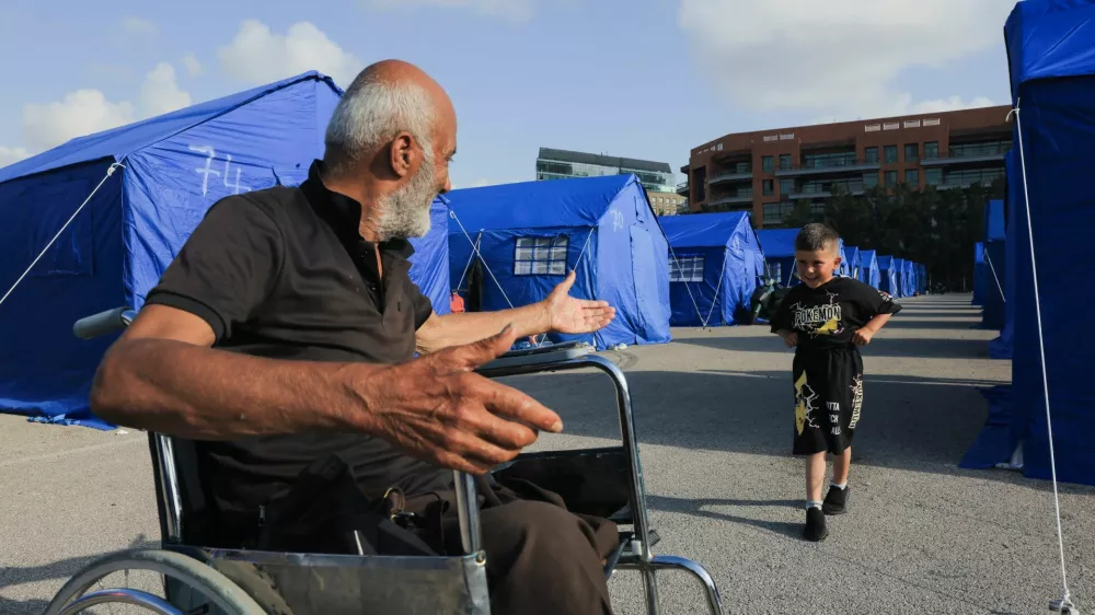 Mohamad Saaydoun, 69, displaced from Beirut's southern suburbs, suffering from injuries after he survived an Israeli strike when he was fleeing home, who had previously lost part of his leg due to diabetes and a medical condition and later lost the rest of his leg in the strike, plays with his grandchild outside his tent at the Beirut waterfront, in Beirut, Lebanon, May 21, 2026. REUTERS/Raghed Waked