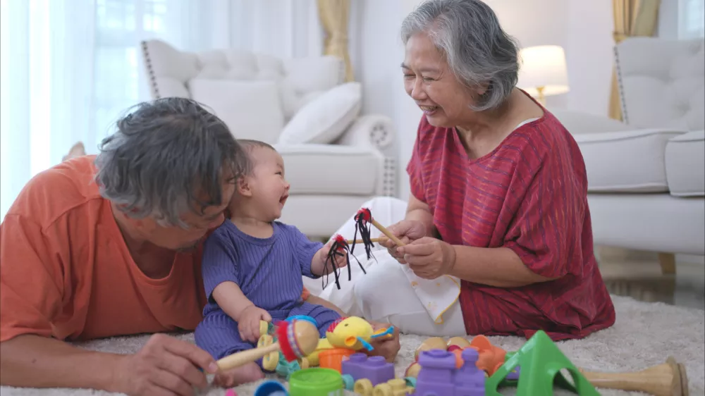 Grandparents and their little grandchild play happily in the living room of the house