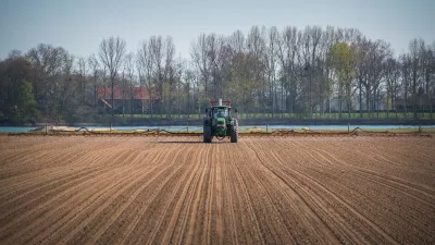 A tractor driving in the middle of arable land against trees and blue sky