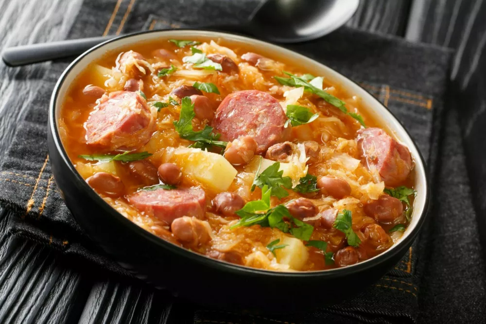 Portion of Jota sauerkraut with borlotti beans, potatoes and sausages close-up in a bowl on the table. horizontal / Foto: Alleko