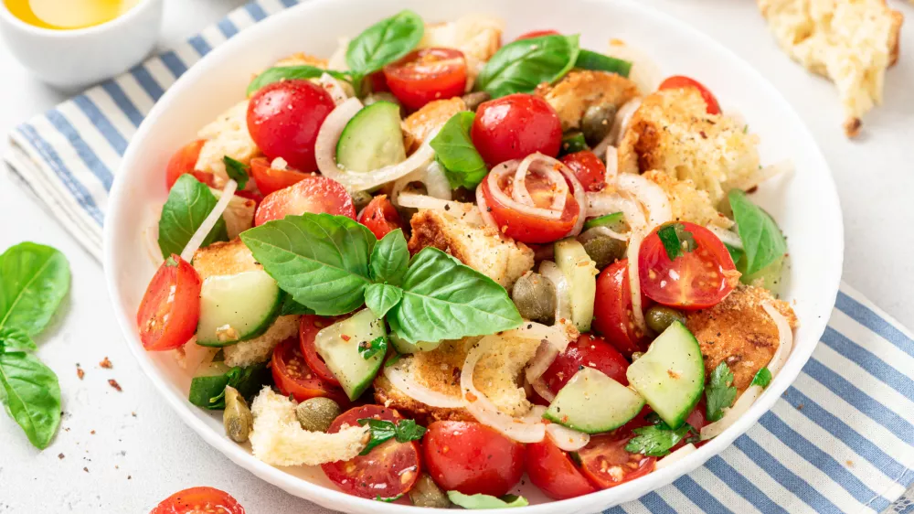 Panzanella - Italian salad from vegetables and bread. Salad with tomatoes, onions, cucumbers, bread, capers and basil in a white plate on a gray concrete background. Vegan salad, Italian cuisine / Foto: Svetlana Monyakova