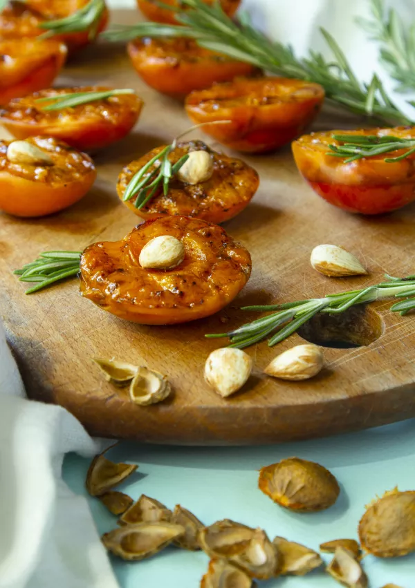 Summer dessert. Ripe grilled peaches with Apricot kernels and rosemary leaves on wooden cutting board on light background. / Foto: Iggi_boo
