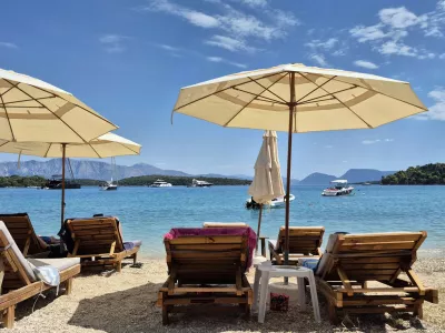 Serene beach scene with wooden loungers and sun umbrellas facing a calm, turquoise sea with boats under a bright blue sky, ideal for summer and vacation themes.