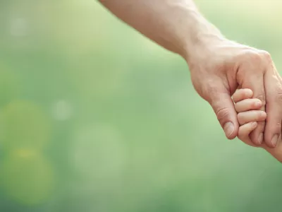 Fathers hand holding his little child in sunny day outdoor, united family and happy childhood concept, banner format with copy space.