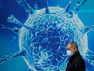 FILE PHOTO: A man wearing a protective face mask walks past an illustration of a virus outside a regional science centre, as the city and surrounding areas face local restrictions in an effort to avoid a local lockdown being forced upon the region, amid the coronavirus disease (COVID-19) outbreak, in Oldham, Britain August 3, 2020. REUTERS/Phil Noble/File Photo / Foto: Phil Noble