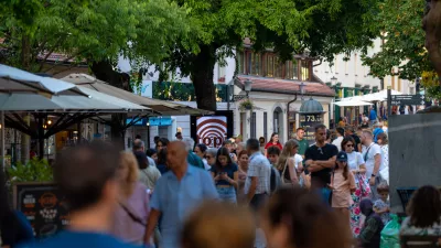 Capturing the lively atmosphere of a European summer, this shot shows a bustling pedestrian street in Ljubljana's historic center. Crowds of tourists and locals stroll past outdoor cafes and shops shaded by large trees. The warm natural light and vibrant urban energy make it ideal for travel guides, city lifestyle features, and tourism marketing showcasing popular destinations in Slovenia.