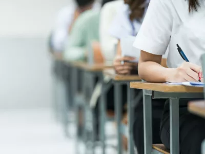 Students Taking Exam in Classroom Setting. Students in uniforms are seated in a classroom, writing answers during an exam, highlighting focus and academic testing.