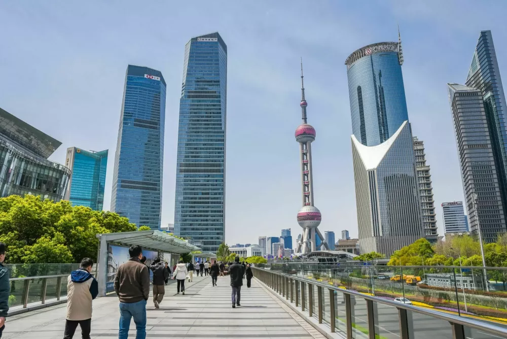Shanghai, China - 1 April 2025: A wide-angle view of Pudong's waterfront promenade with the Oriental Pearl Tower dominating the skyline, modern designer benches in the foreground, and crowds enjoying the sunny spring day. / Foto: Tatiana Terekhina