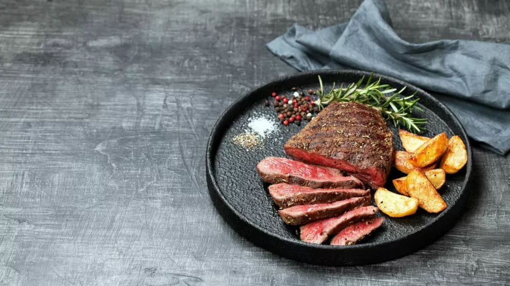Sliced medium rare grilled beef steak and potato wedges, selective focus / Foto: Laperla_foto