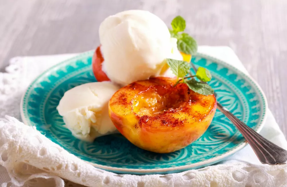 Grilled peaches and ice cream dessert over blue plate / Foto: Manyakotic