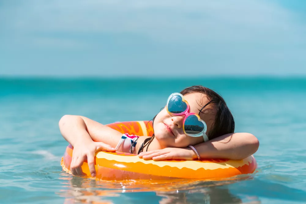 Portrait of Little Asian child girl in swimwear and sunglasses with swim ring playing in the sea in summer sunny day. Happy children kid enjoy and fun outdoor lifestyle travel ocean on beach holiday vacation. / Foto: Candyretriever Getty Images
