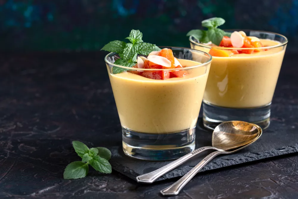 Homemade dessert of milk, cream and fresh peaches in glasses served with fresh mint and peach slices, selective focus. Concept of creamy fruit desserts. / Foto: Smarina