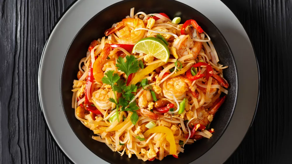 pad thai, phad thai, stir-fried rice noodles with shrimps, peanuts, scrambled eggs, bean sprouts, spring onion, red pepper, lime, in black bowl on black table, free space, flat lay, close-up / Foto: From_my_point_of_view