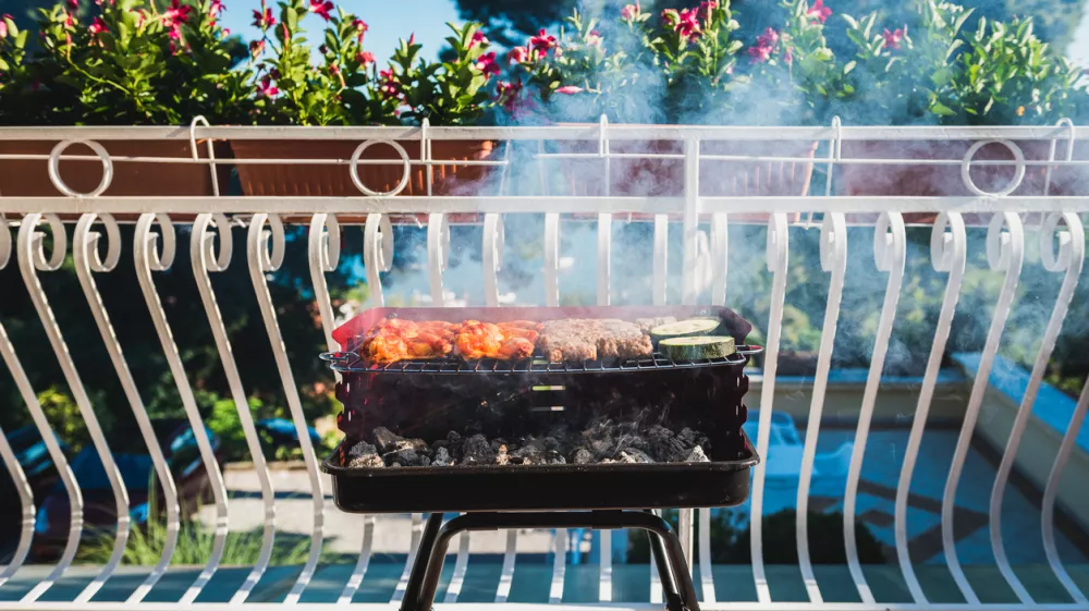 Delicious meat on barbecue grill with coal on balcony. Grilling food on a balcony or a terrace with wonderful view. Small cheap BBQ grill at home. / Foto: _jure Getty Images/istockphoto