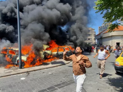 People run in front of burned cars that were attacked in an Israeli airstrike in the southern port city of Sidon, Lebanon, Wednesday, June 10, 2026. (AP Photo/Mohammed Zaatari)