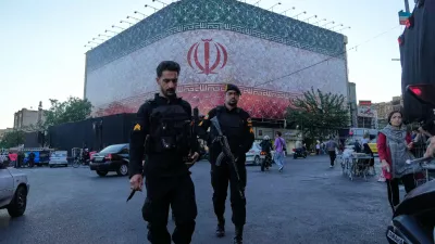 Policemen walk in front of a huge banner showing Iranian flag at the Islamic Revolution square in Tehran, Iran, Sunday, June 14, 2026. (AP Photo/Vahid Salemi)