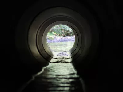 View through a round concrete tunnel carrying a stream beneath a road