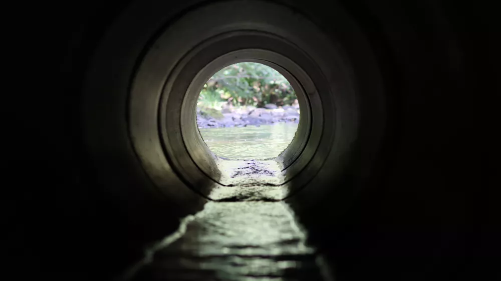 View through a round concrete tunnel carrying a stream beneath a road
