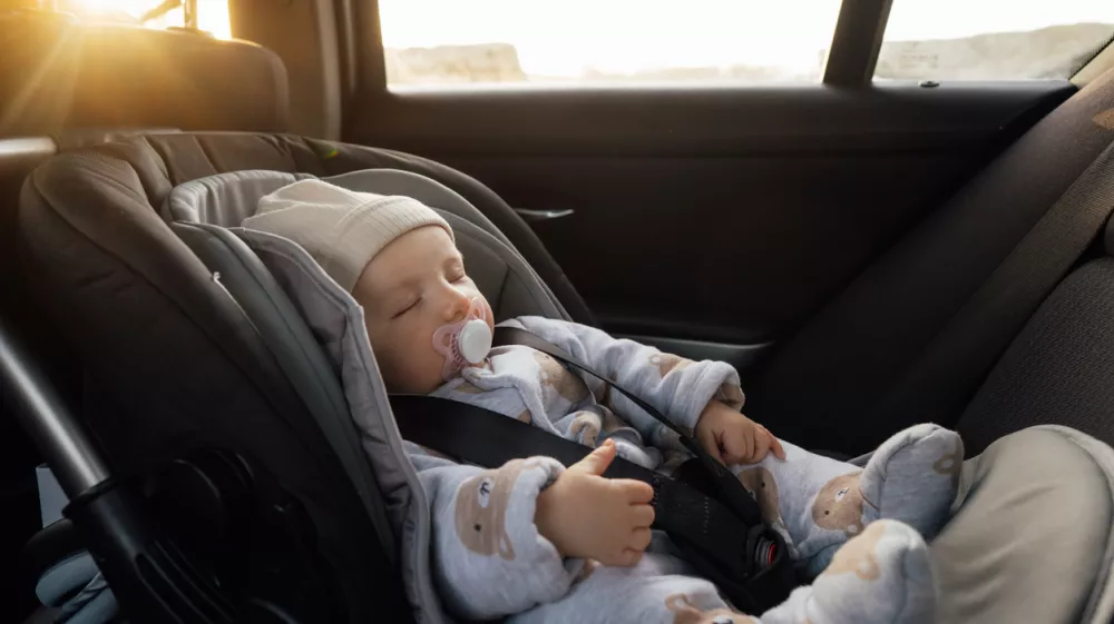 Baby sleeping in an infant car seat, safety travelling by car with little child. Little baby fastened with seat belt in safety car seat. Road trip lifestyle child care transportation rear-facing.