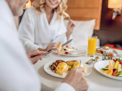 Breakfast time. A couple in white robes having breakfast and looking pleased / Foto: Oleksandr But Getty Images