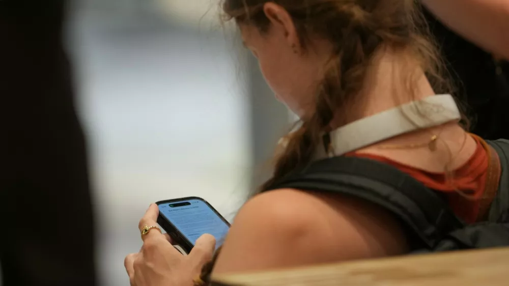 A teenager looks at her mobile phone in London, Monday, June 15, 2026. (AP Photo/Kin Cheung)