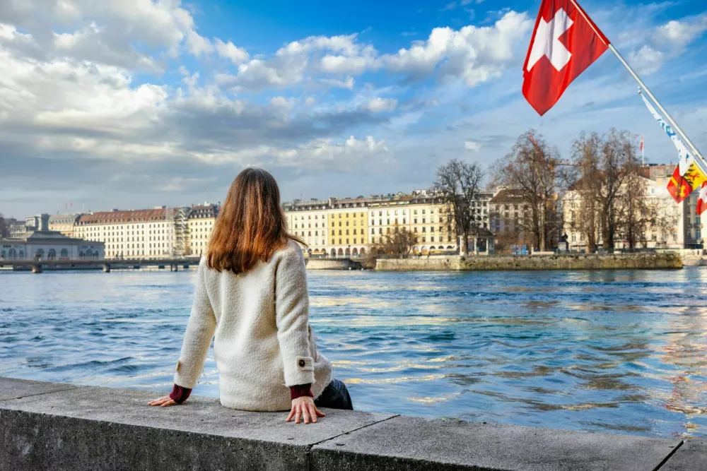 A tourist woman looks at the beautiful view of the cityscape of Geneva, Switzerland, with River Rhone and lake during a sunny winter day / Foto: Shansche