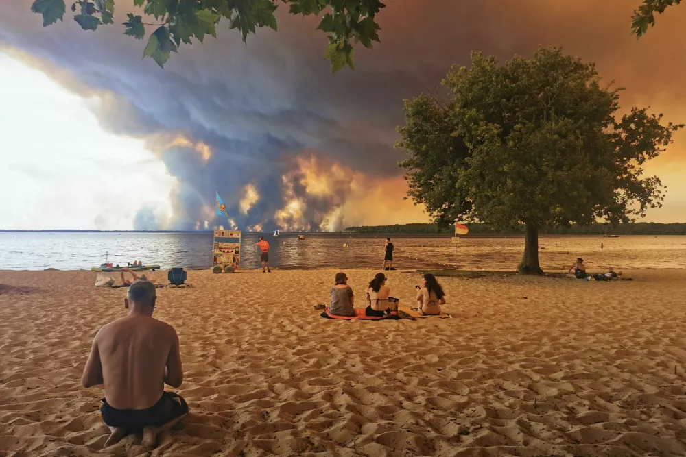 Beach goers rest on the beach of Moutchic on the shore of Lake Lacanau (Etang de Lacanau) in Lacanau, southwestern France on July 24, 2026, as clouds of smoke rise into the sky from the Gironde wildfire. The fire raging in the northern part of the Arcachon Basin in Gironde, southwest France, has swept through more than 3,400 hectares, according to the latest figures released by the prefecture. More than 20,000 residents and tourists have been evacuated from this part already devastated by flames in 2022. Scientists have long warned that climate change caused by human use of fossil fuels will make periods of drought more intense and longer-lasting, creating the ideal conditions for wildfires.,Image: 1118261819, License: Rights-managed, Restrictions:, Model Release: no / Foto: Profimedia