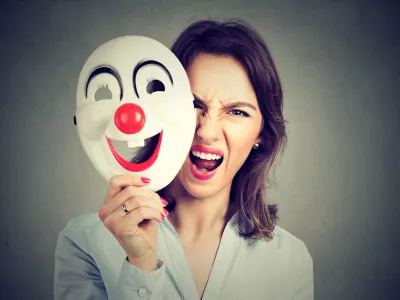 Portrait angry screaming woman taking off happy clown mask isolated on gray wall background. Negative human emotions feelings / Foto: Siphotography