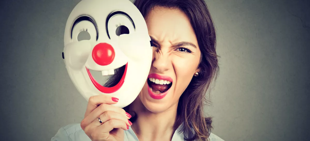 Portrait angry screaming woman taking off happy clown mask isolated on gray wall background. Negative human emotions feelings / Foto: Siphotography