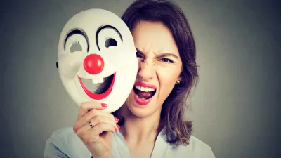 Portrait angry screaming woman taking off happy clown mask isolated on gray wall background. Negative human emotions feelings / Foto: Siphotography