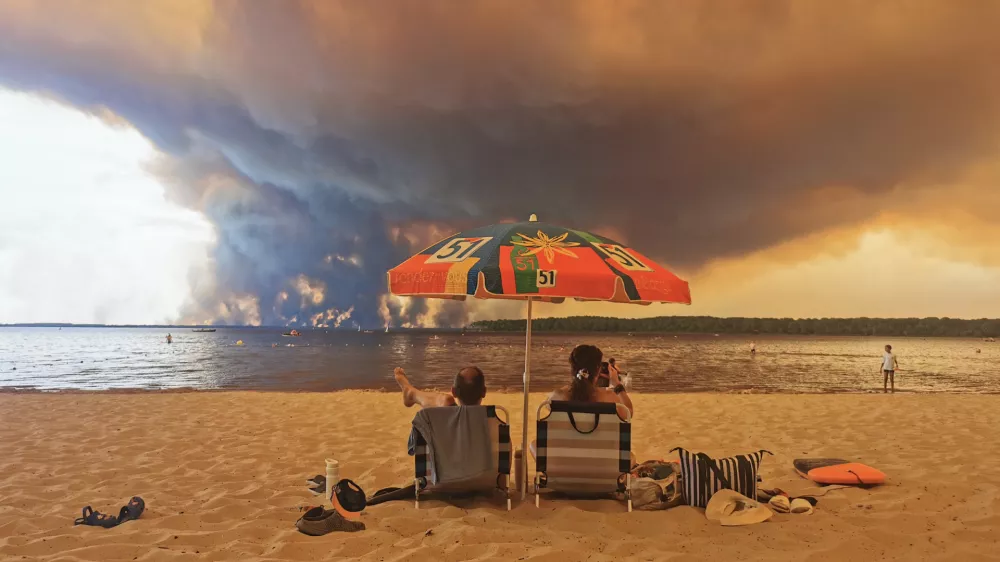 Beach goers rest on the beach of Moutchic on the shore of Lake Lacanau (Etang de Lacanau) in Lacanau, southwestern France on July 24, 2026, as clouds of smoke rise into the sky from the Gironde wildfire. The fire raging in the northern part of the Arcachon Basin in Gironde, southwest France, has swept through more than 3,400 hectares, according to the latest figures released by the prefecture. More than 20,000 residents and tourists have been evacuated from this part already devastated by flames in 2022. Scientists have long warned that climate change caused by human use of fossil fuels will make periods of drought more intense and longer-lasting, creating the ideal conditions for wildfires.,Image: 1118260144, License: Rights-managed, Restrictions:, Model Release: no / Foto: Profimedia