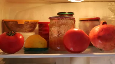 Food items, including bright tomatoes, a lemon, and a pomegranate, sit on a glass shelf inside a refrigerator next to homemade preserves in jars. This close-up shot illustrates food storage and supplies inside the kitchen appliance. / Foto: Oleh Strus Getty Images