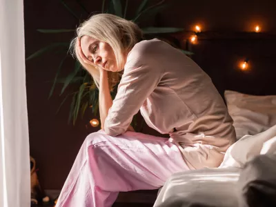Upset middle-aged woman sit on bed in bedroom lost in thoughts thinking pondering of problem solution, depressed unhappy mature female look in distance suffer from depression, having personal problems