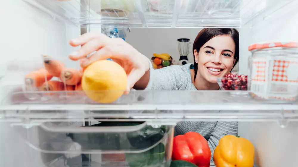 Smiling woman taking a fresh lemon out of the fridge, healthy food concept
