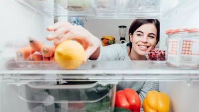 Smiling woman taking a fresh lemon out of the fridge, healthy food concept