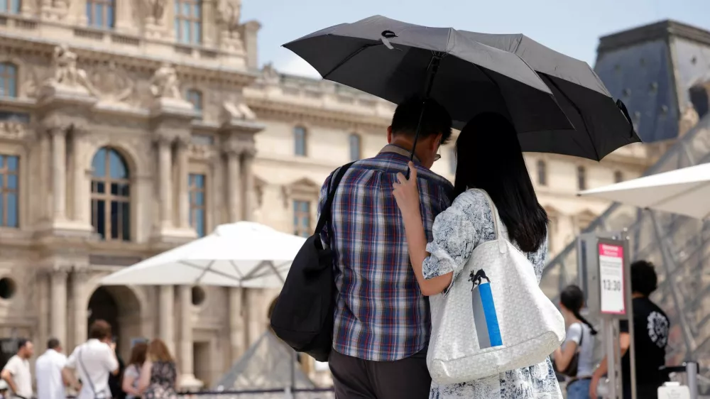 Tourists protecting themselves from the sun under umbrellas stand in front of the Pyramid of the Louvre Museum as temperatures rise in Paris during a second heatwave affecting a large of France, June 19, 2026. REUTERS/Alice Sacco