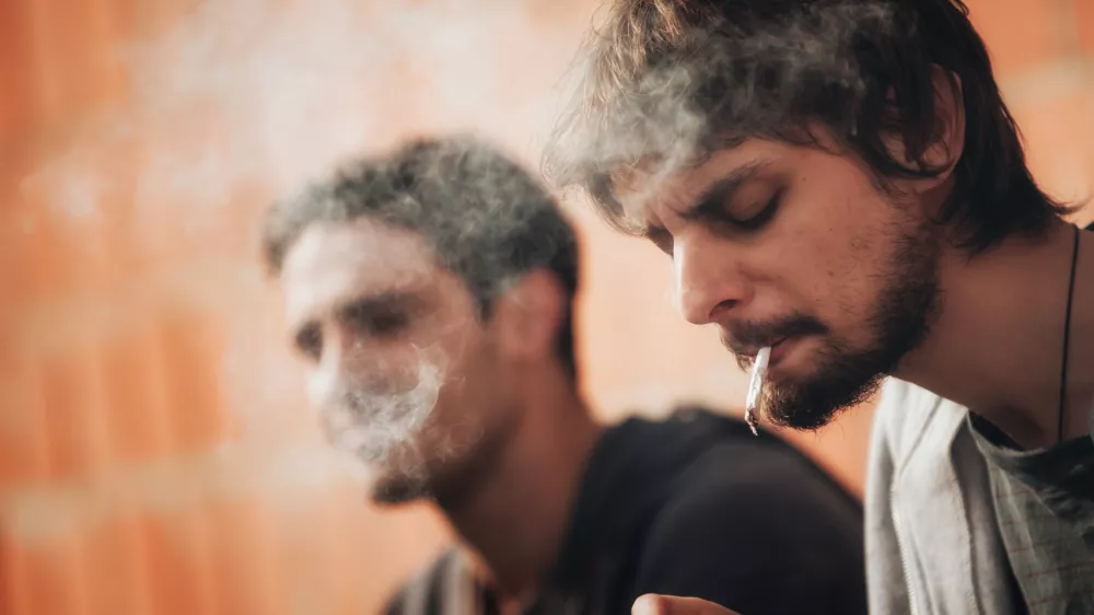 Closeup of young friends smoke pot or hashish joint in abandoned ghetto part of the city