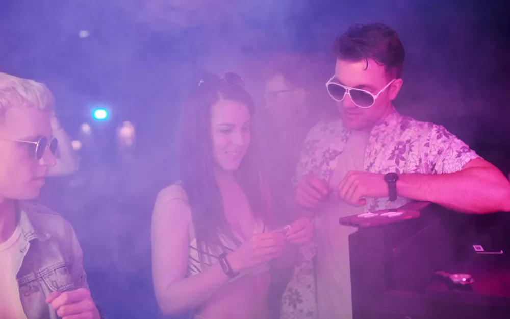 Young people sniffing drug in nightclub with colorful laser lights.