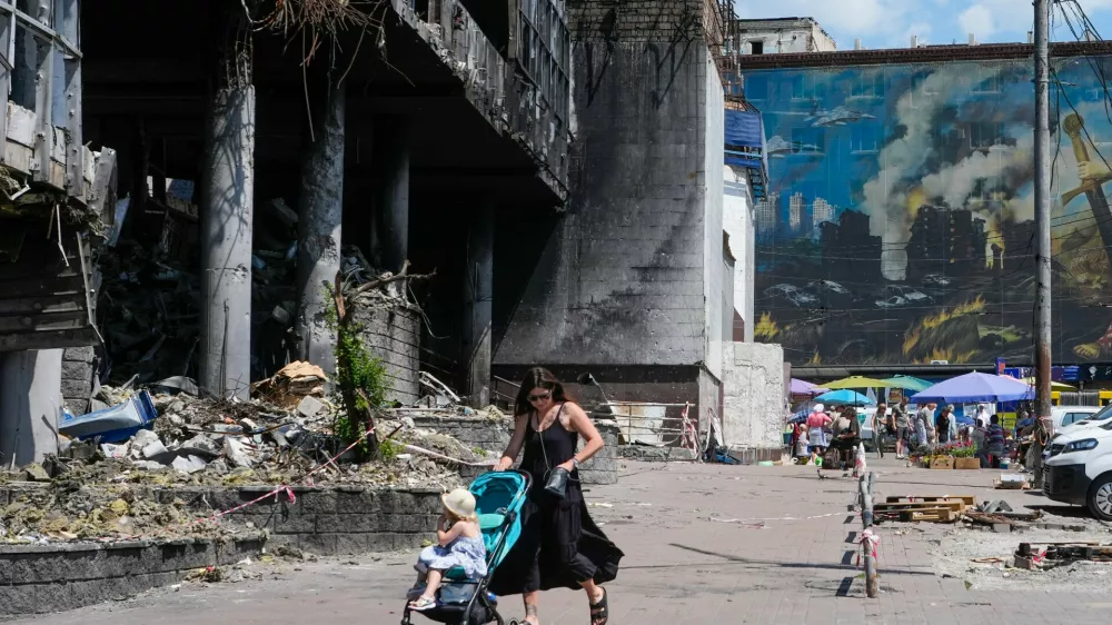 A mother pushes a stroller past a damaged building covered with street artist paintings and a big city marketplace that was destroyed recently by Russian missiles in Kyiv, Ukraine, Monday, June 22, 2026.(AP Photo/Efrem Lukatsky)
